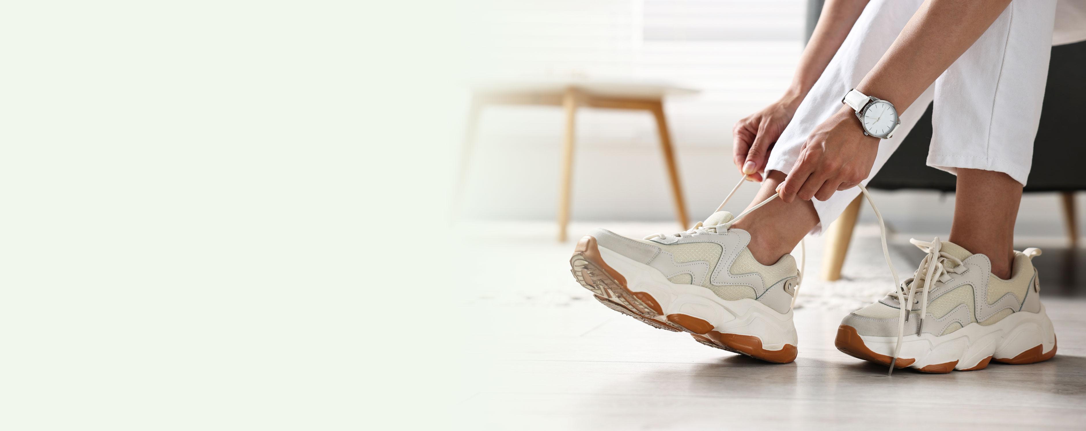 Sfeerbeeld van een vrouw die haar modieuze witte comfortsneakers aantrekt, ontworpen voor optimale ondersteuning.