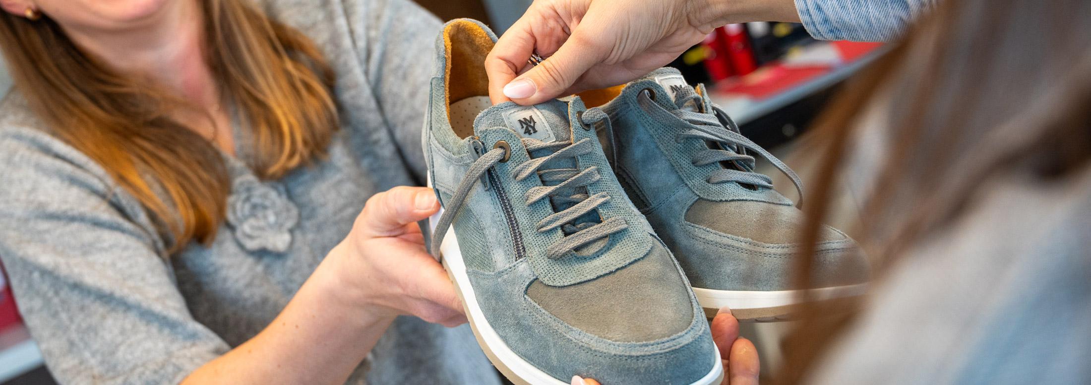 Gros plan d\'un technicien orthopédiste ajustant les lacets d\'une chaussure de confort en daim bleu sur mesure.